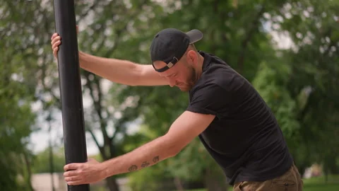 Individual Carefully Aligning Pole In Park Environment, Person Wearing Backwards Stock Footage 330898663