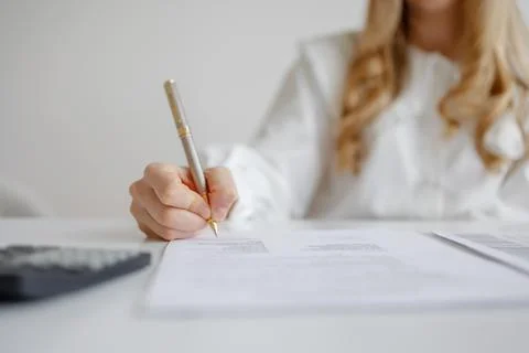 Individual completing paperwork with pen while sitting at desk with calculator Stock Photos