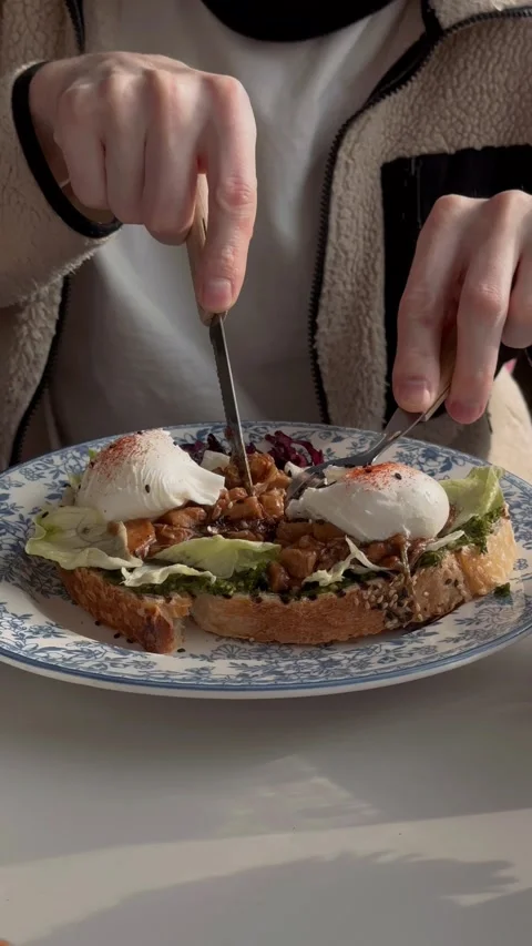 Individual cutting soft poached eggs on toast during breakfast 動画素材 333332832