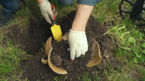 Individual digs in soil with a small shovel, uncovering a buried ceramic pot Stock Footage 337511994
