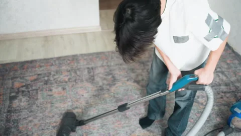 Individual diligently cleans patterned carpet with blue vacuum cleaner Stock Footage 345536324