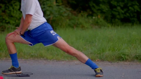 Individual doing calf and hamstring stretch on roadside in outdoor setting Видео 321029870