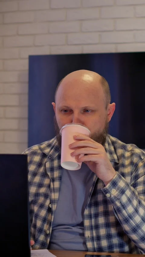 Individual enjoying coffee break at computer. Male seated at workspace sipping Stock-Footage 344718214