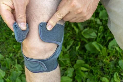 Individual is fitting a knee support on their right knee while standing on .. Stock Photos