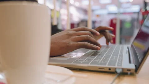 Individual focused on computer amidst lively coffee shop environment. Remote 스톡 동영상 333182645