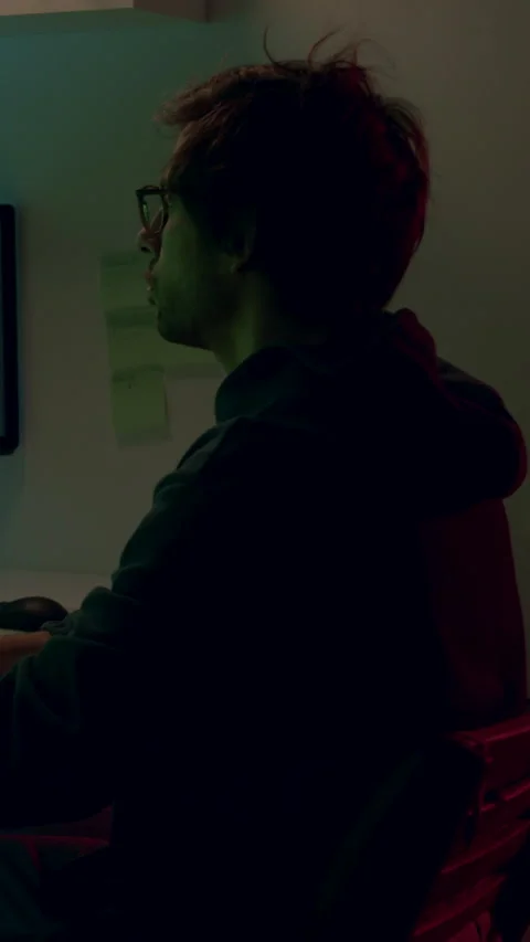 Individual focused on multiple computer screens displaying green data and Stock Footage 313928878