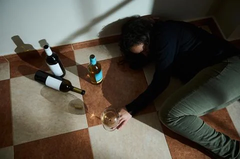 Individual lying on tiled floor surrounded by empty wine bottles Stock Photos