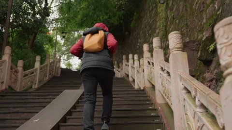 Individual navigating rugged mossy temple staircase calmly. Adventurer in red Stock Footage 345164922