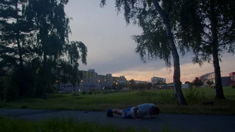 Individual pauses during exercise beneath evening sky and trees Stock Footage 324591914