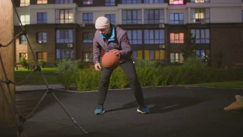 Individual player practicing basketball under city lights at night, Solitary Stock Footage 329454916