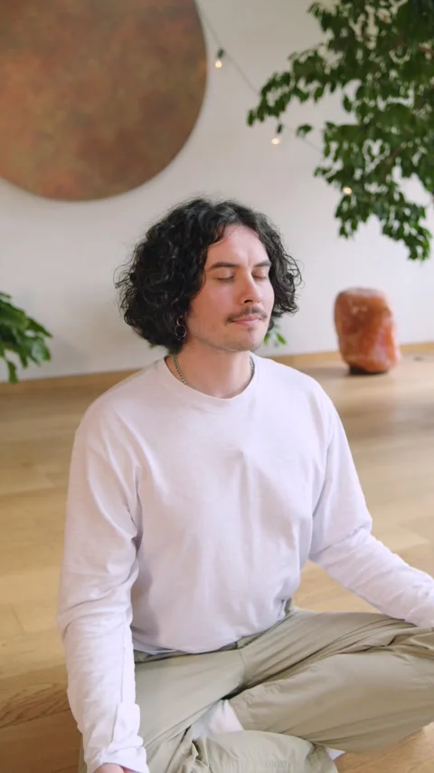 Individual practices meditation in a bright room surrounded by green plants and  Stock Footage 346149717
