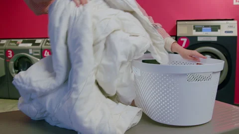 Individual prepares a large white comforter for washing at a self-service Stock Footage 328105142