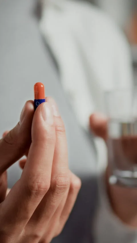 Individual preparing to take a capsule with a glass of water in a bright set Stock Footage 331601499