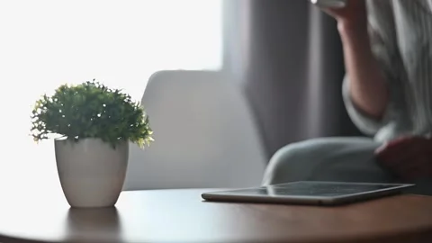 Individual seen holding a drink while seated at a table. A tablet is on the 스톡 동영상 336778532