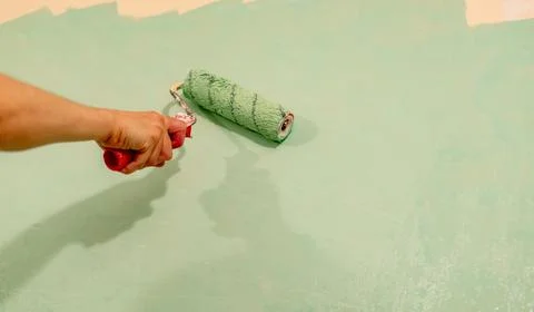 Individual using a paint roller to apply green paint on a wall, demonstrating Stock Photos