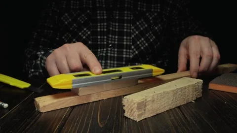 Individual using a yellow level tool to measure wooden planks on a dark wooden Stock Footage 329619724