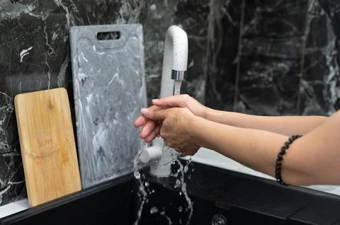 An individual washes their hands under a stylish faucet, reflecting hygiene i Stock Photos