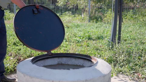 Individual in work attire opens a sewer manhole cover, revealing the interior Stock Footage 318709264