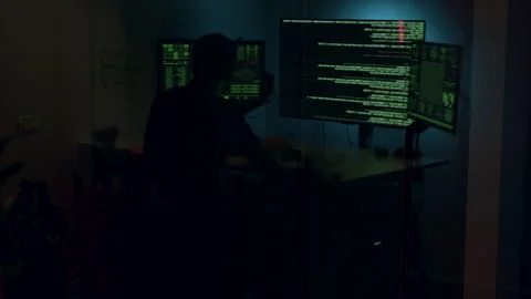 Individual working intently in a dark tech lab, surrounded by glowing screens Stock Footage 322549421