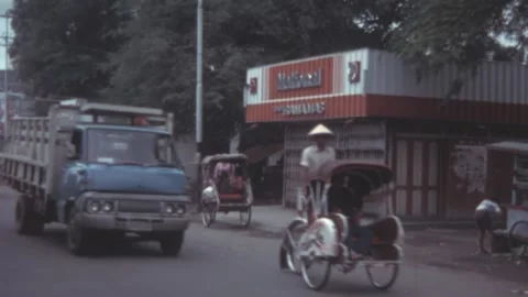 Indonesia - 1981: Becak driver pedals down a busy city street with vintage cars Video stock 285315942
