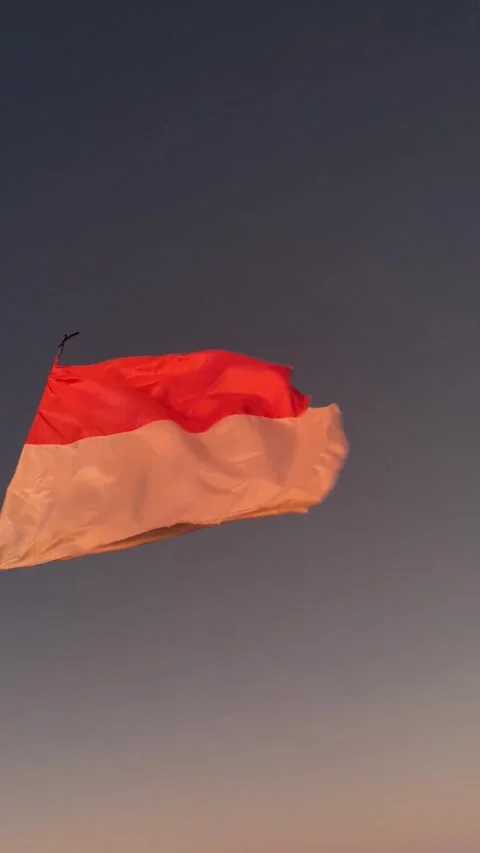 The Indonesian flag gracefully waves against the backdrop of a dusky sky. Stockbeeldmateriaal 332260003