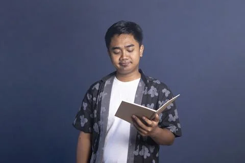 Indonesian man looking down at an open notebook with a calm, disappointed, .. Stock Photos