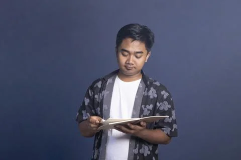 Indonesian man looking down while turning the page of an open notebook, che.. Stock Photos