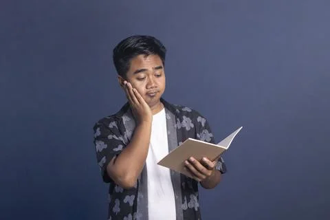 Indonesian man looking at an open notebook with one hand on his cheek, feel.. Stock Photos