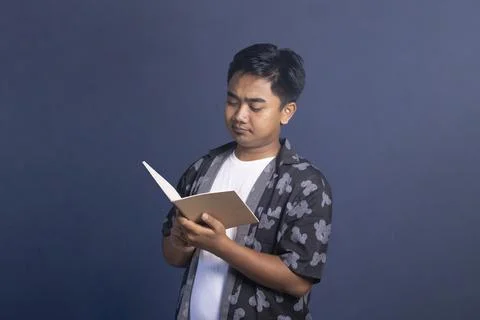 Indonesian man standing while holding and seriously reading an open noteboo.. Fotos de archivo