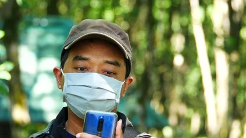 Indonesian man wearing a blue surgical face mask and using a mobile phone. 4K Stock Footage