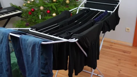 Indoor clothes drying rack with jeans and dark laundry on a wooden floor Stock Footage 325361741