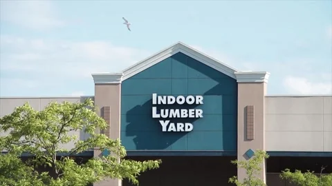 Indoor lumber yard sign on storefront with tree in front and sky and clouds Stock Footage 249098932