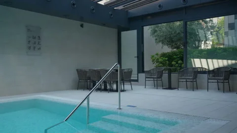Indoor spa pool lounge area with dining table and panoramic garden view windows Stock Footage 345714048