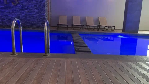 Indoor swimming pool with blue lighting, metal ladder, and wooden deck at m.. Stock Footage 333130445