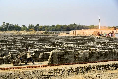 Industrial Brick Yard With Stacks Of Bricks And A Worker Pushing A Wheelbarro Stock Photos