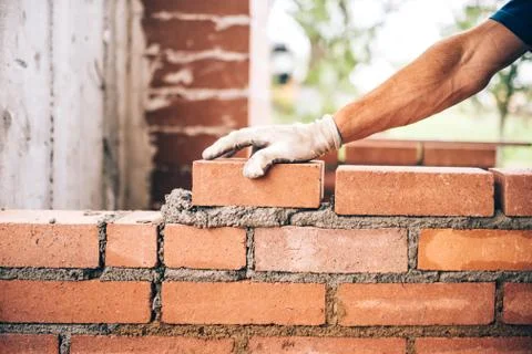 Industrial bricklayer worker placing bricks on cement while building exterior Stock Photos