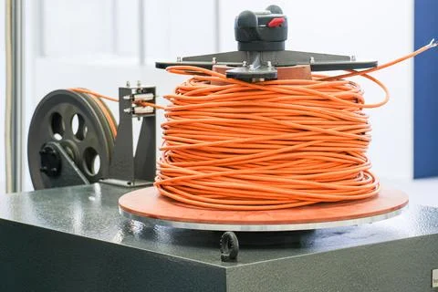Industrial cable winding machine with orange electric wire on reel. Stock Photos