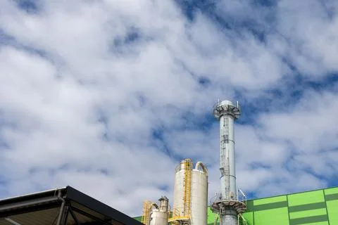 Industrial chimney tower and processing tanks under cloudy sky 库存照片
