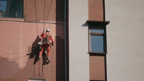 Industrial climber applying protective coating or paint to building facade Stock Footage 303523011