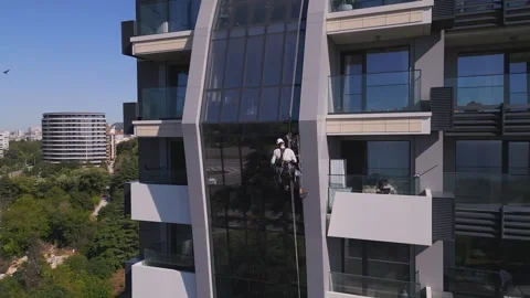 Industrial climber performs tasks at a great height on a glass wall of a tall Video stock 246921196