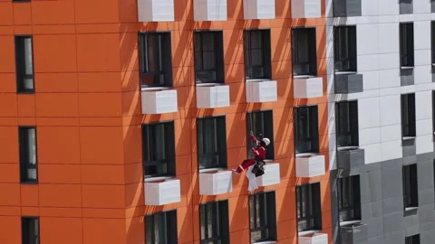 Industrial climber rappels down along the orange facade of residential building Stock Footage 278843560