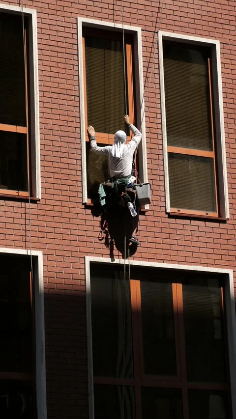 An industrial climber washes windows on the facade of a multi-story building Stock Footage 344471080