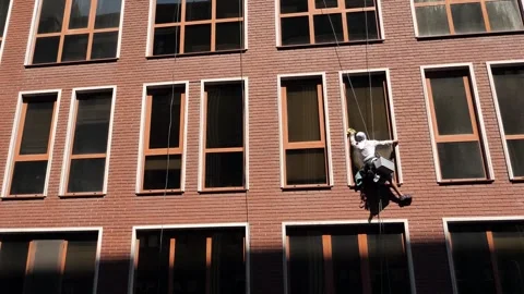 An industrial climber washes windows on the facade of a multi-story building Stock Footage 344471595