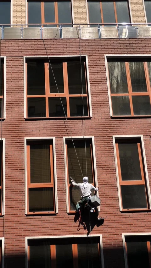 An industrial climber washes windows on the facade of a multi-story building Stock Footage 344472435