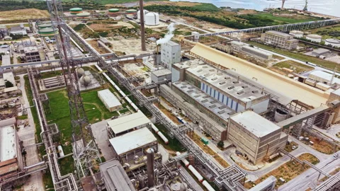 Industrial complex with multiple buildings and pipelines located near water on a Stock Footage 341604281