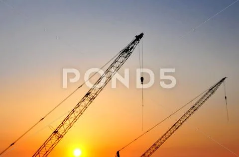 Industrial construction cranes and building silhouettes over sun at sunrise. Stock Photos