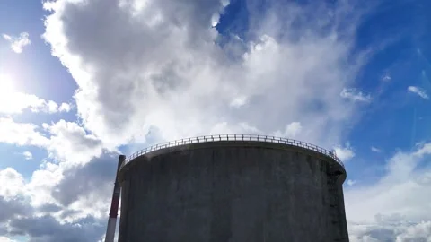 Industrial cooling tower emits steam against the background of a blue sky with Stock Footage 341472425