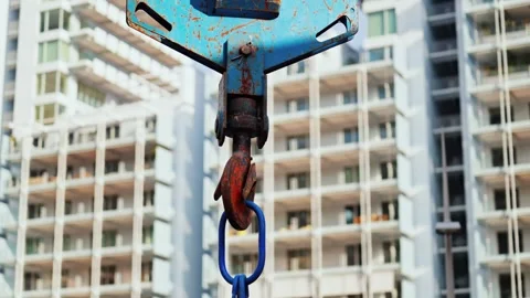 Industrial crane hook with blue chain link moves against background of tall.. Stock Footage 339346813