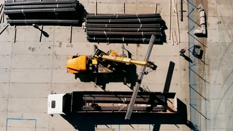 An industrial crane loads a section of Drilling pipes into a truck bed, Aerial Stock Footage 153147388