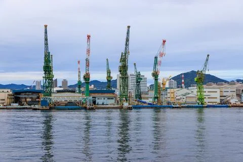 Industrial cranes at cargo loading dock at quiet harbor on cloudy day Stock Photos